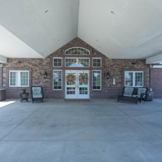 The image shows the entrance of a brick building with multiple windows and seating arrangements outside.
