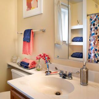 A neatly arranged bathroom with colorful towels, a floral arrangement, and a decorative painting above the towel rack.