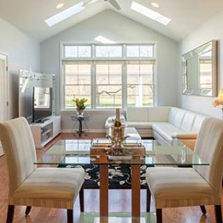 A modern living room with a glass dining table, comfortable seating, and abundant natural light from large windows.