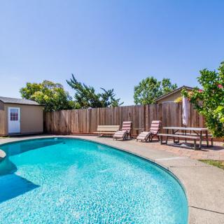 A sunny backyard featuring a swimming pool with lounge chairs and a wooden fence.