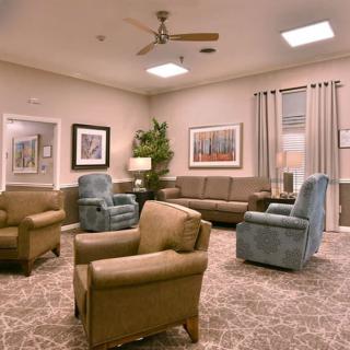 A comfortable living room with sofas and armchairs arranged around a carpeted floor, decorated with artwork and plants.