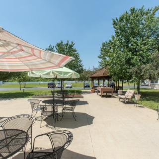 A sunny outdoor patio area with tables, chairs, and umbrellas near a gazebo surrounded by lush greenery.
