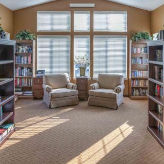 A cozy reading room with bookshelves and comfortable chairs bathed in sunlight.