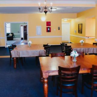 A cozy dining area with wooden tables and chairs, adorned with simple floral decorations under warm lighting.