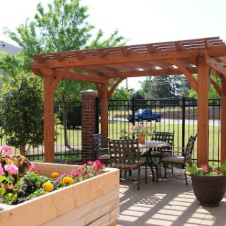 A serene outdoor patio area featuring a wooden pergola, seating arrangements, and vibrant flower beds.