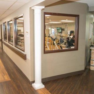 A corridor in a rehabilitation center featuring gym equipment visible through large windows.