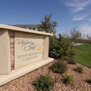 A welcoming sign for an active adult retirement community, surrounded by landscaping and greenery.