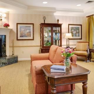 A cozy living room with a sofa, table, and fireplace, adorned with artwork and a vase of flowers.