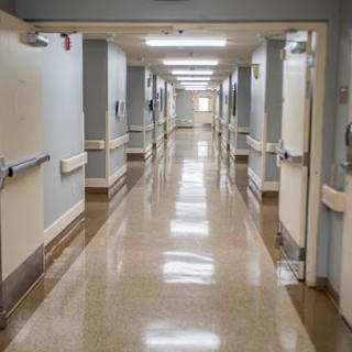 A long, clean corridor within a hospital, featuring doors on either side and bright overhead lighting.