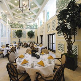 An elegant dining area with round tables, neatly arranged table settings, and decorative plants in a luxurious restaurant interior.