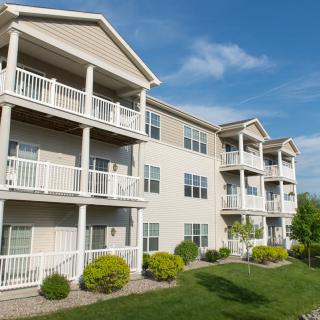 A multi-story apartment building with balconies and landscaped surroundings under a clear blue sky.