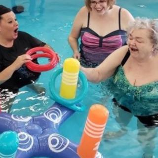 Three women enjoy a fun pool game with colorful floating toys.