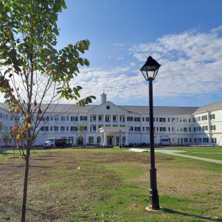 A wide view of a school building with a lamp post and tree in the foreground on a sunny day.