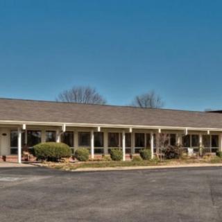 A single-story motel with a parking lot in front, featuring a row of columns along its facade.