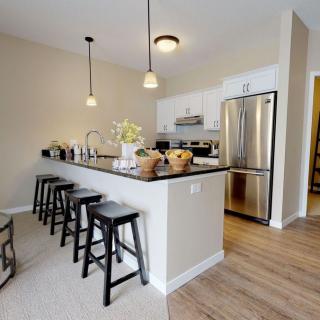 A modern kitchen with a sleek design, featuring stainless steel appliances, an island counter with bar stools, and elegant pendant lighting.