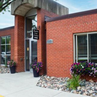 A brick building with a modern entrance, featuring large windows and decorative plants outside.