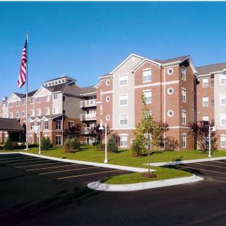 A residential apartment building with a parking lot and an American flag in front.