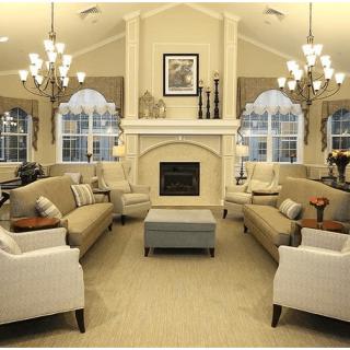 A cozy and elegant living room featuring a central fireplace, multiple sofas, large windows, and chandeliers.