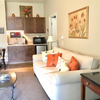 A cozy living area featuring a white sofa with colorful pillows, a small kitchenette, and decorative artwork.