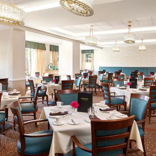 A spacious and elegantly decorated restaurant dining room with neatly set tables and wooden chairs.