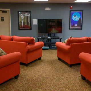 A cozy lounge area with red sofas arranged around a television, complemented by wall art and a carpeted floor.