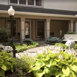 A tranquil courtyard featuring lush greenery, a bench, and a lamp post.