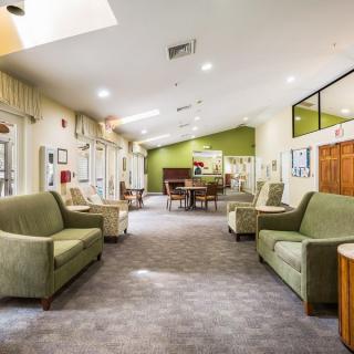 A spacious and well-lit lounge area with green sofas, modern decor, and a carpeted floor.