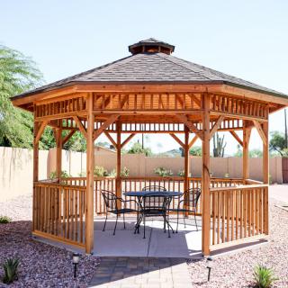 A charming wooden gazebo in a garden setting with patio furniture.