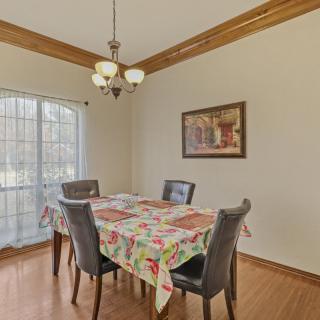 A well-lit dining area with a table covered in a floral tablecloth, surrounded by four chairs. A chandelier hangs above and a painting decorates the wall.