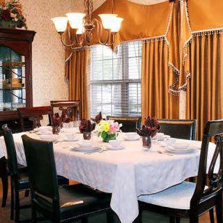 A formal dining room with an elegantly set table, featuring a chandelier and gold curtains.