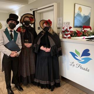 Three people in period costumes and masks stand by a reception desk.