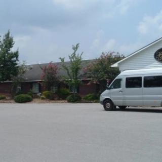 A silver van parked in front of a building with a cloudy sky overhead.