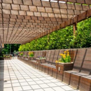 A wooden pergola with seating and planters in an outdoor garden setting.