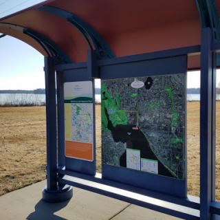 A bus stop featuring a detailed map, situated near a scenic area by the water.