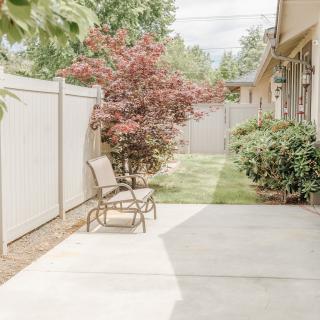 A serene backyard patio with outdoor seating, surrounded by lush greenery and a privacy fence.