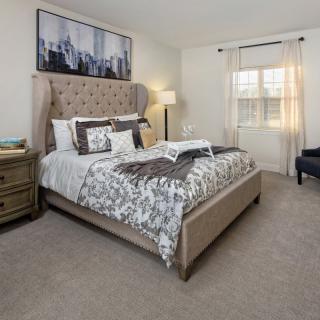 A cozy and elegantly decorated bedroom featuring a plush bed, bedside table, floor lamp, and a window with light curtains.