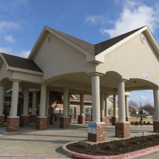 A modern building with a prominent entrance featuring columns and a large overhang on a sunny day.