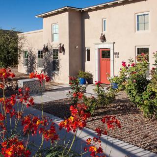 A stucco house with a vibrant garden featuring red and orange flowers in a desert landscape.