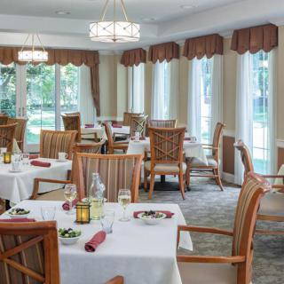 An elegant dining room with tables and wooden chairs, set near large windows with curtains, offering a pleasant ambiance.