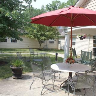 A cozy backyard patio with a red umbrella and outdoor furniture on a sunny day.