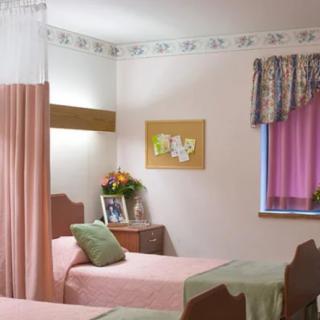 A hospital room with twin beds, decorative curtains, and a bedside table with flowers.
