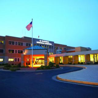 A healthcare facility illuminated at dusk, featuring an American flag at the entrance.