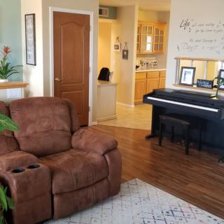 A cozy living room with a recliner, piano, and indoor plants on wooden flooring.