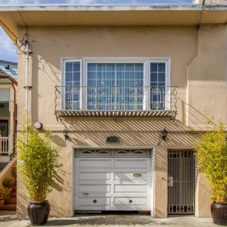A two-story house with a garage and large windows, flanked by potted plants.
