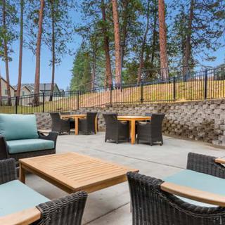 A cozy outdoor patio area with comfortable seating and tables, surrounded by trees.