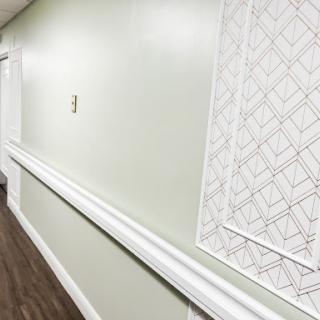 A well-lit hallway featuring green walls, a decorative panel, and wooden flooring.