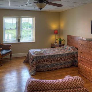 A cozy bedroom with a bed, wooden dresser, and a large window providing natural light.