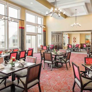 A spacious and elegantly designed dining room with large windows, chandeliers, and well-arranged tables and chairs.