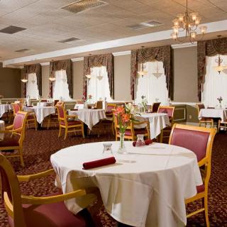 An elegant dining room with neatly arranged tables and chairs, featuring chandeliers and large windows.