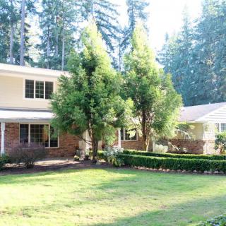 A two-story house surrounded by trees with a well-maintained lawn in a forested area.